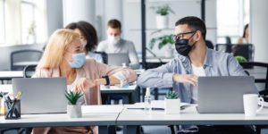 Two office workers at their desk with mask on, talking about the Best company swag for employees