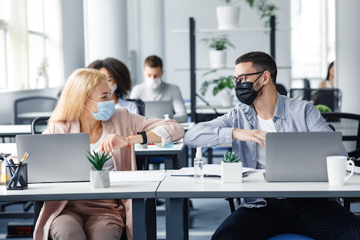 Two office workers at their desk with mask on, talking about the Best company swag for employees