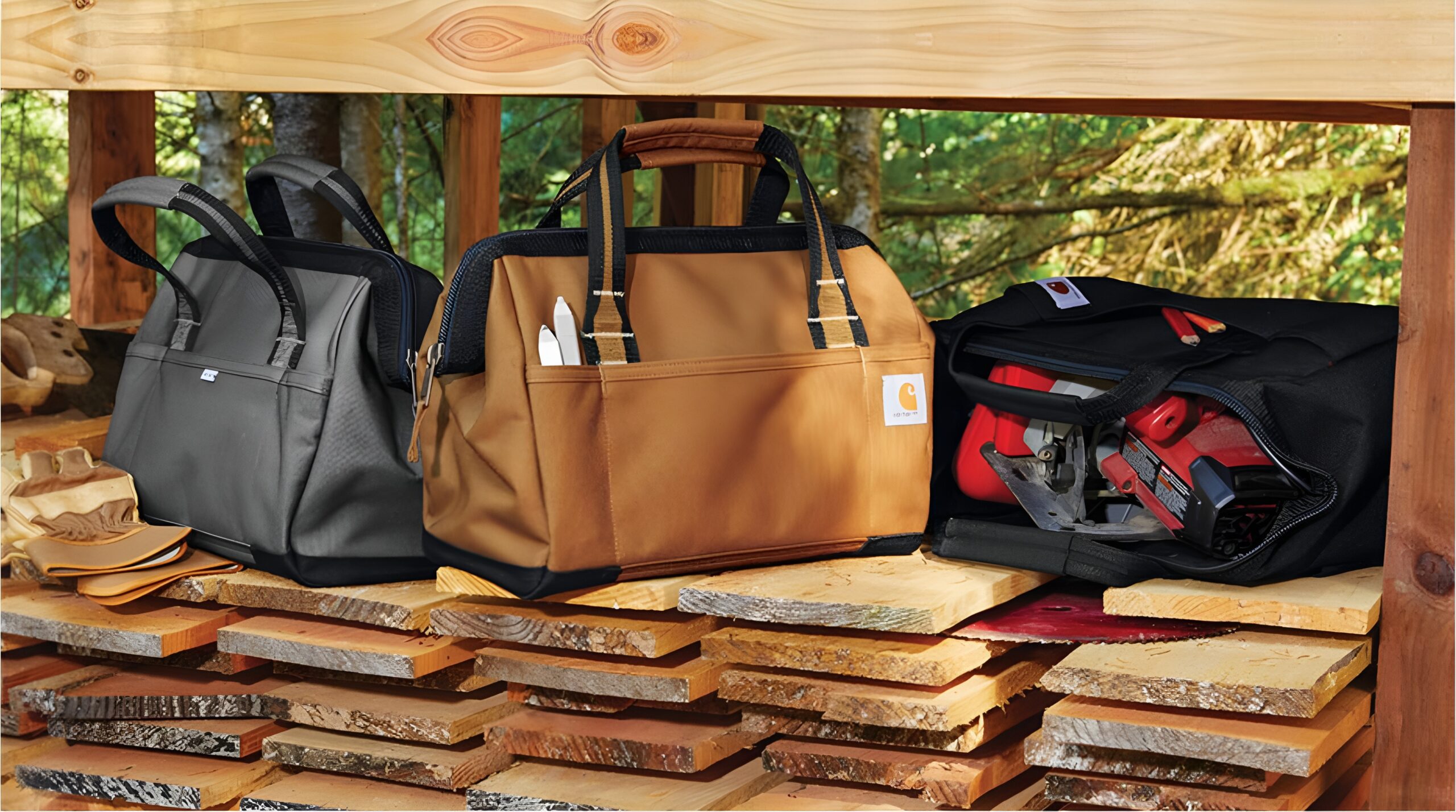RCHQ Carhartt tool bags in black, brown, and loaded with tools sit on wooden planks with gloves beside them.