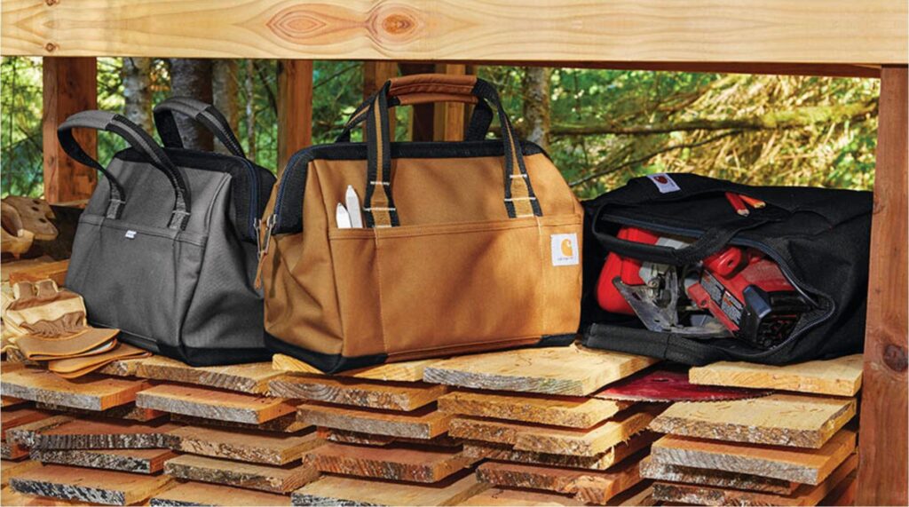 RCHQ Carhartt tool bags in black, brown, and loaded with tools sit on wooden planks with gloves beside them.