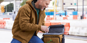 A man sits at a construction site and opens a branded tan lunch cooler bag created by Righteous Clothing Agency.