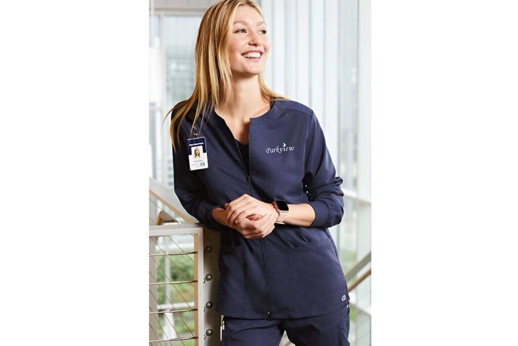 Smiling Parkview healthcare worker in a Righteous navy zip-up uniform jacket and scrubs.