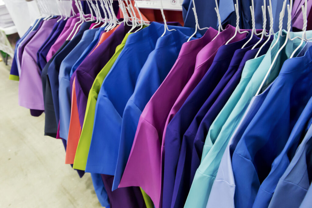 Righteous: A close-up view of vibrant healthcare uniforms in various colors hanging on a clothing rack.