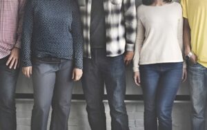 Group of people sporting Righteous apparel standing side by side, shown from shoulders to legs against a neutral wall.