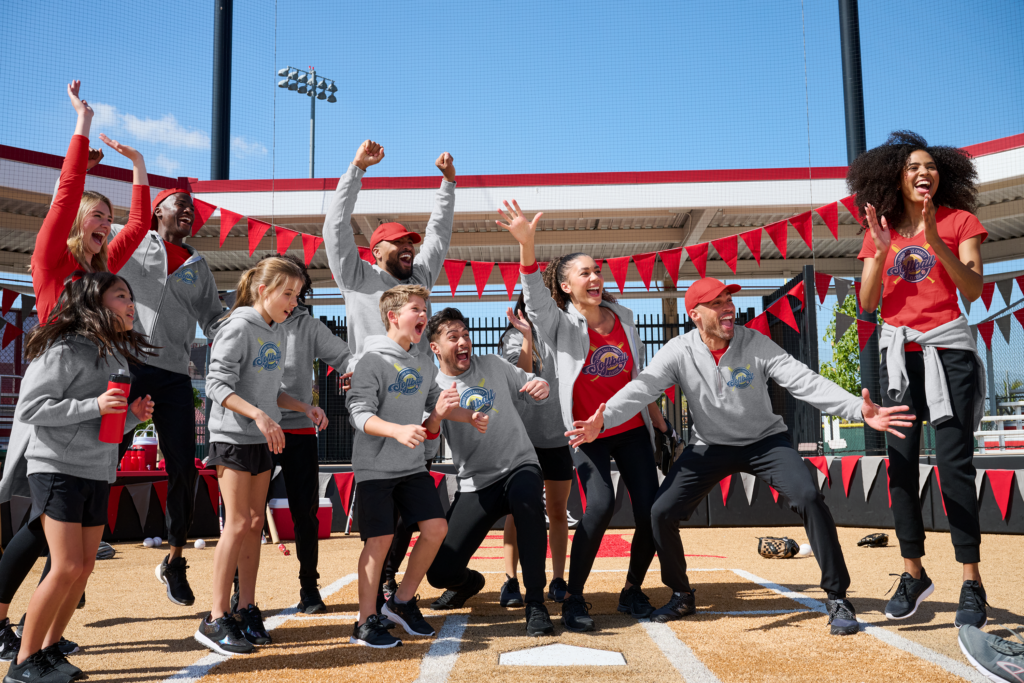 Team cheers in branded hoodies and caps from Righteous Clothing Agency at a softball field event.