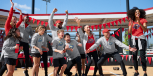 Team cheers in branded hoodies and caps from Righteous Clothing Agency at a softball field event.