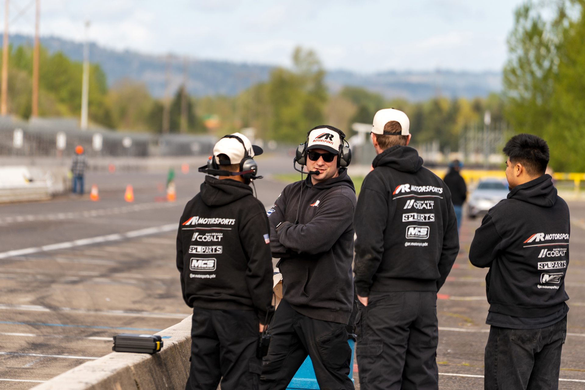 Pit crew members in black hoodies from Righteous Clothing Agency coordinating trackside during a motorsports event.