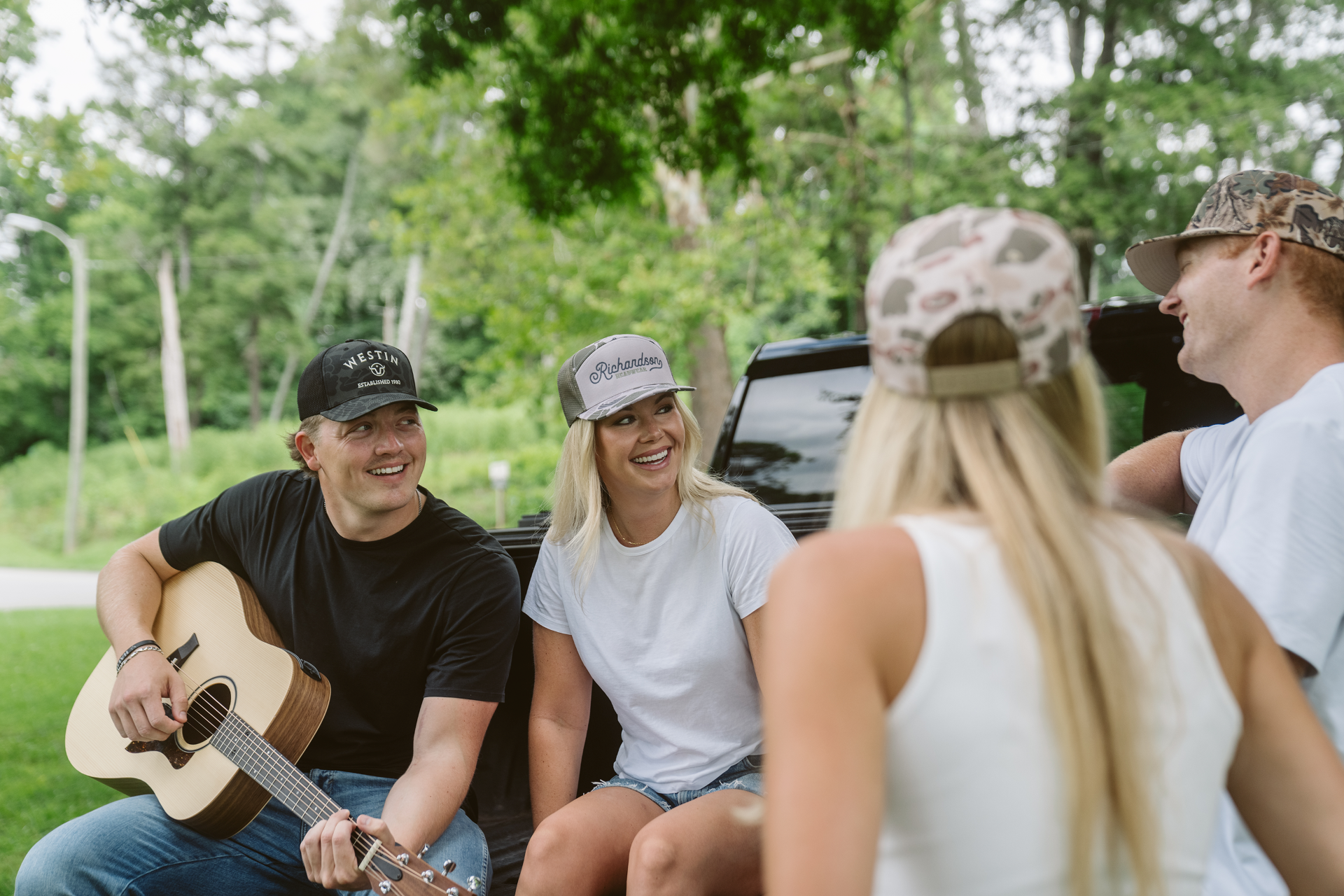 Friends in branded caps chat in a truck bed while one plays guitar, by Righteous Clothing Agency.