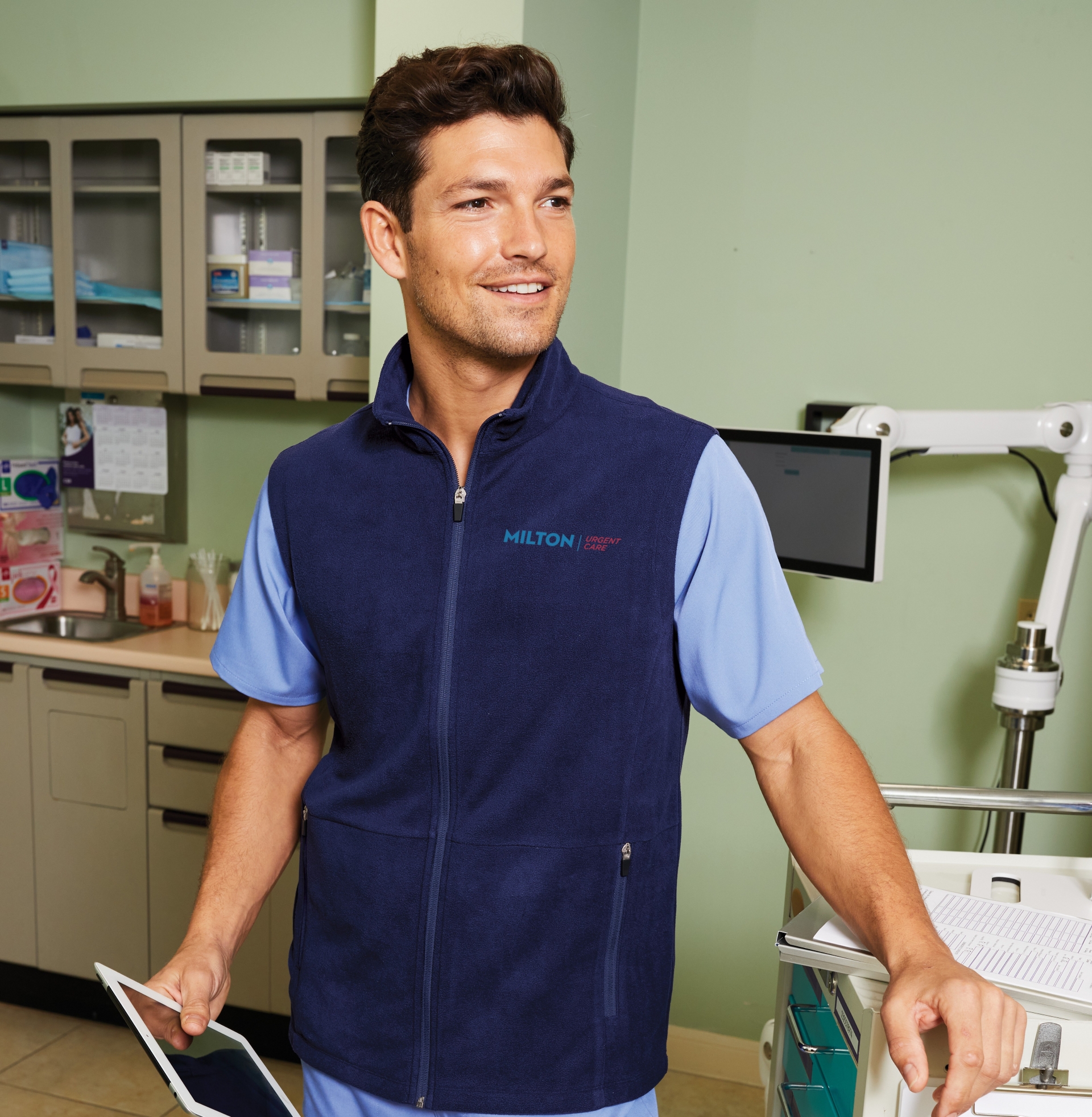 Man in a navy fleece vest with Milton logo, standing in a medical office, wearing Righteous apparel.