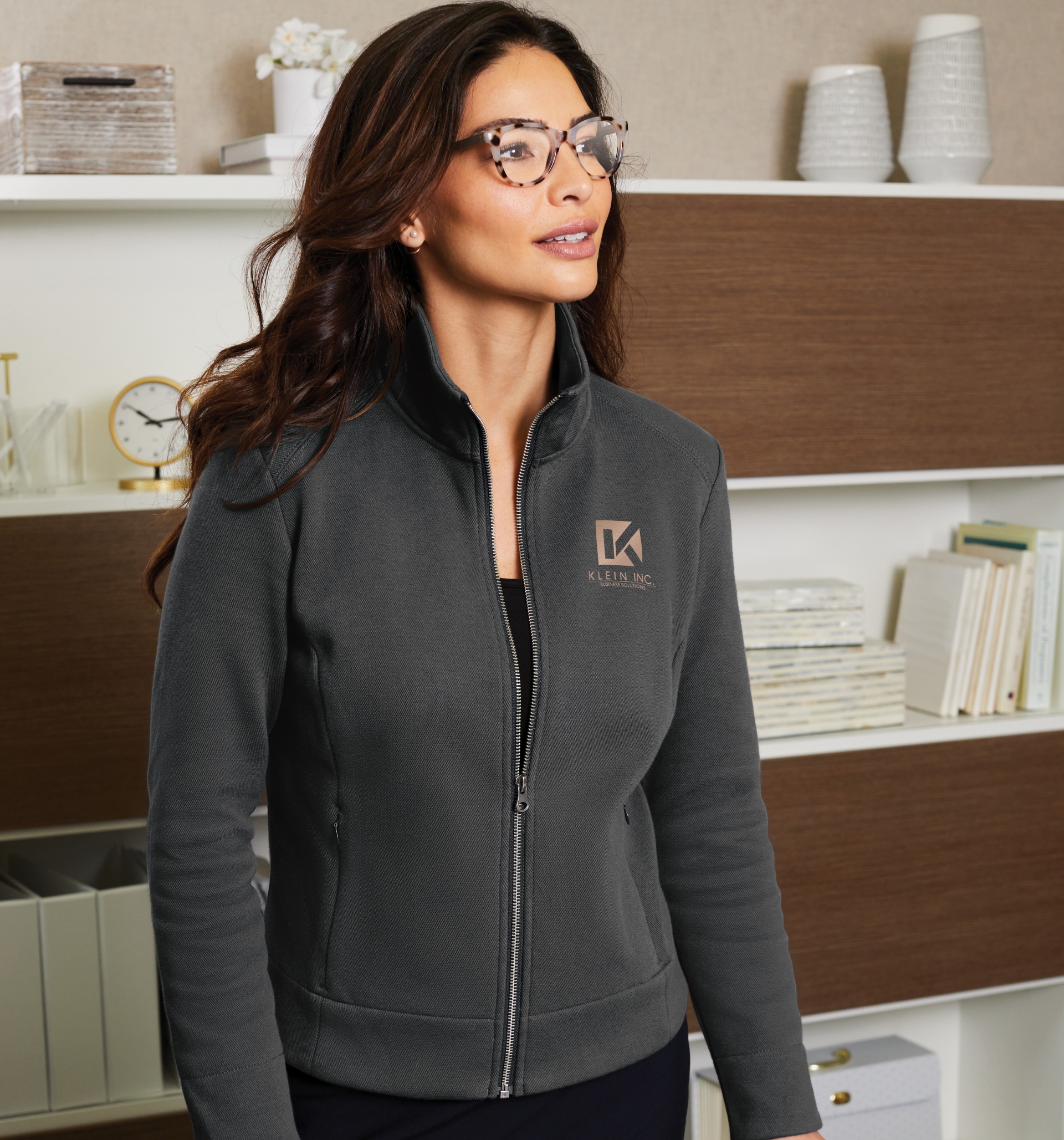 Lifestyle image of a woman in glasses wearing a gray zip-up logo jacket from Righteous indoors.