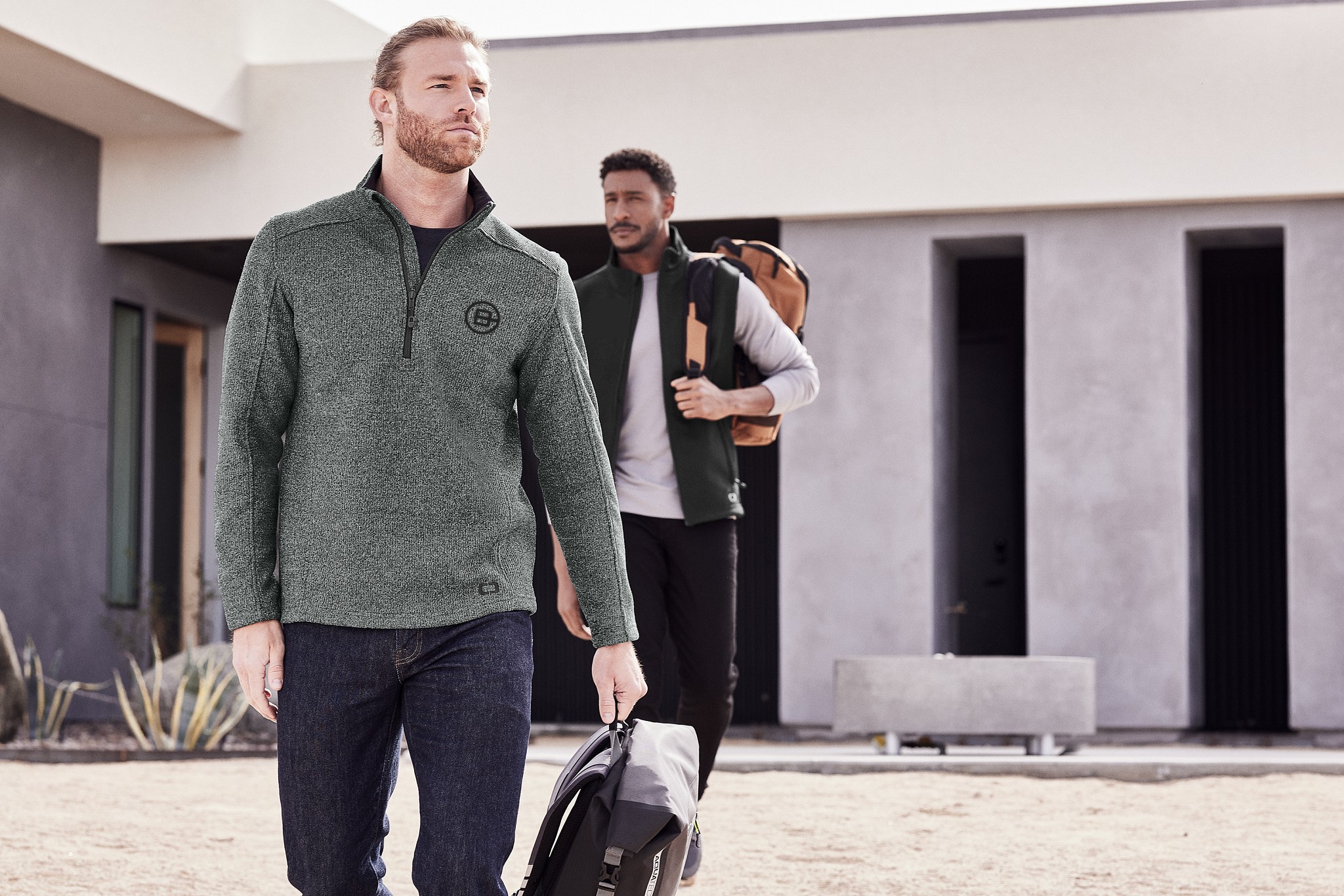 Team members in branded quarter-zip and vest from Righteous, walking outdoors with bags in a modern residential setting.