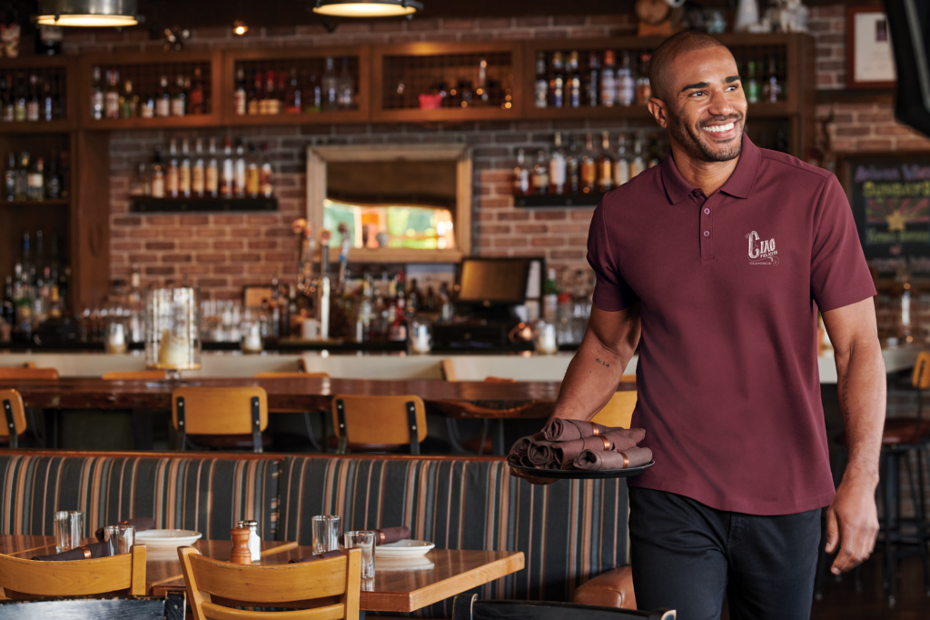 Restaurant server in a branded polo supplied by Righteous Clothing Agency.