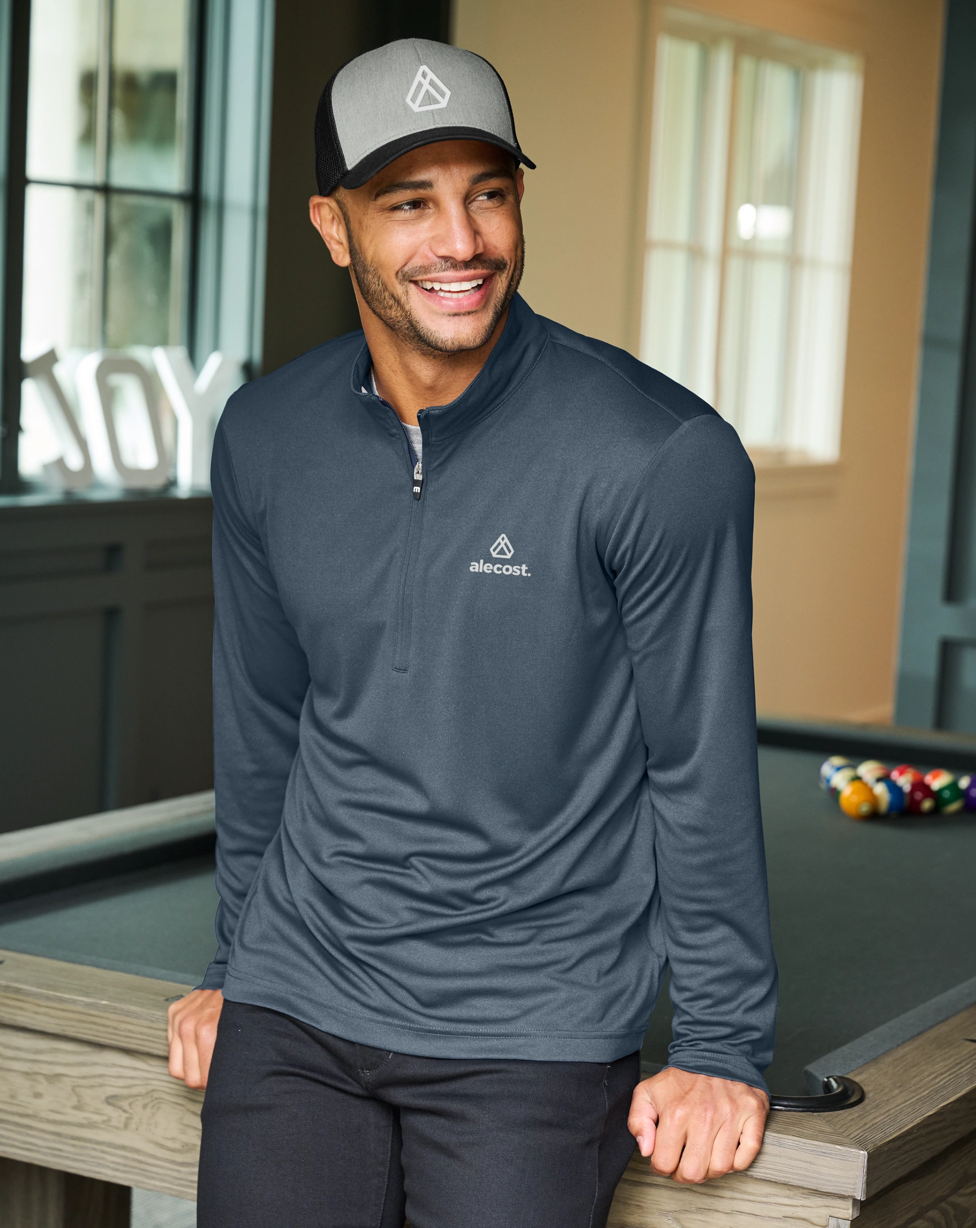 Man in a Righteous custom-branded cap and quarter-zip leans on a pool table. 