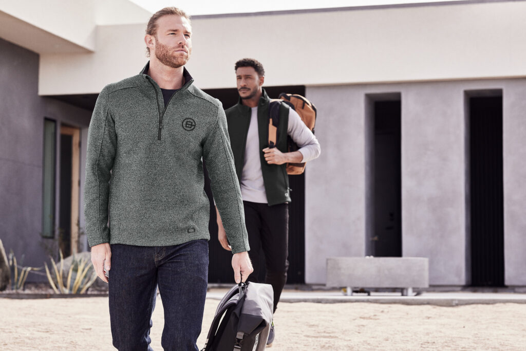 Man wearing a Righteous custom branded quarter zip fleece carrying a backpack while leaving a workplace, representing branded uniforms during a company rebrand transition.