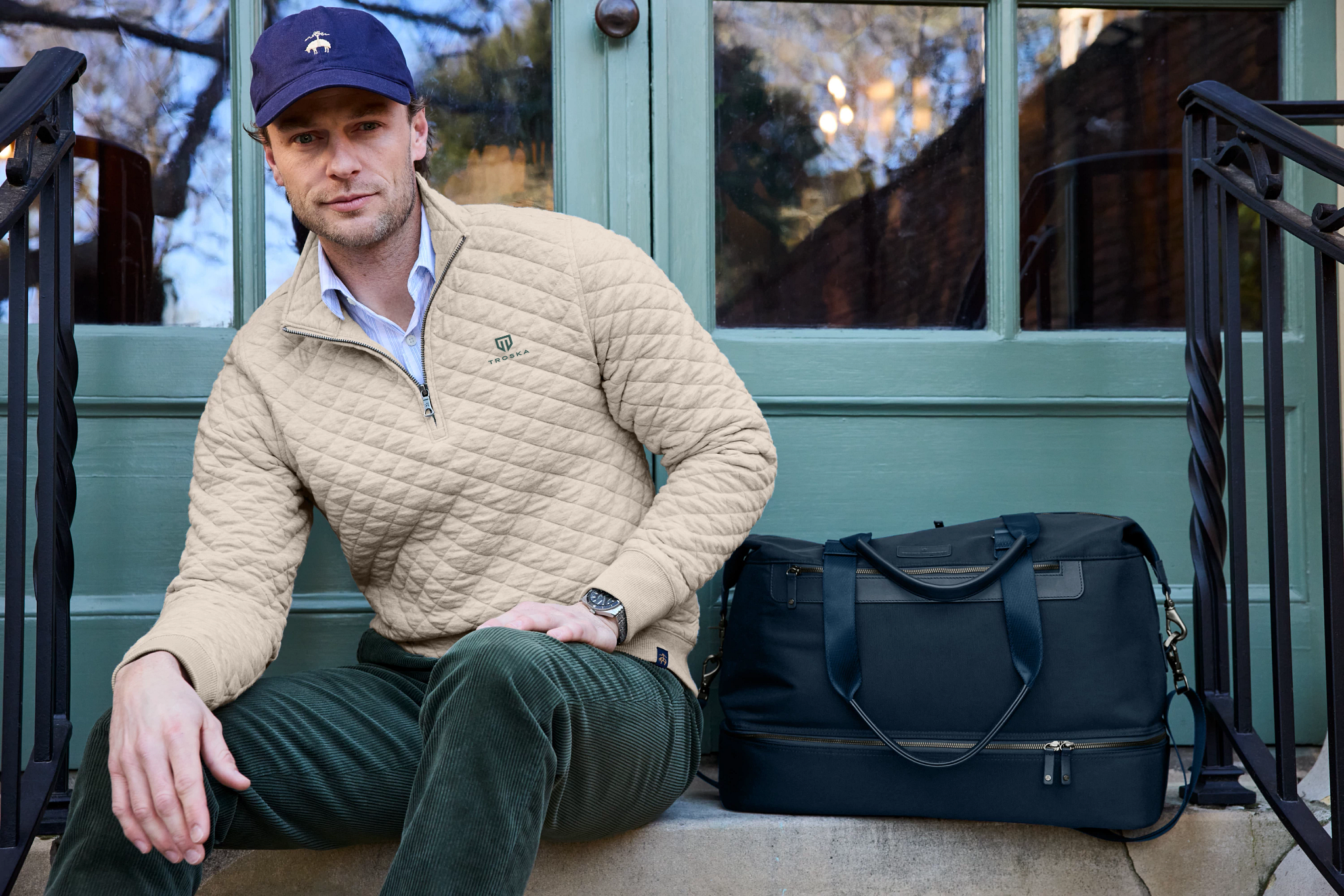 Man in Ra Righteous custom-branded cap and quilted pullover sits beside a navy duffel. 
