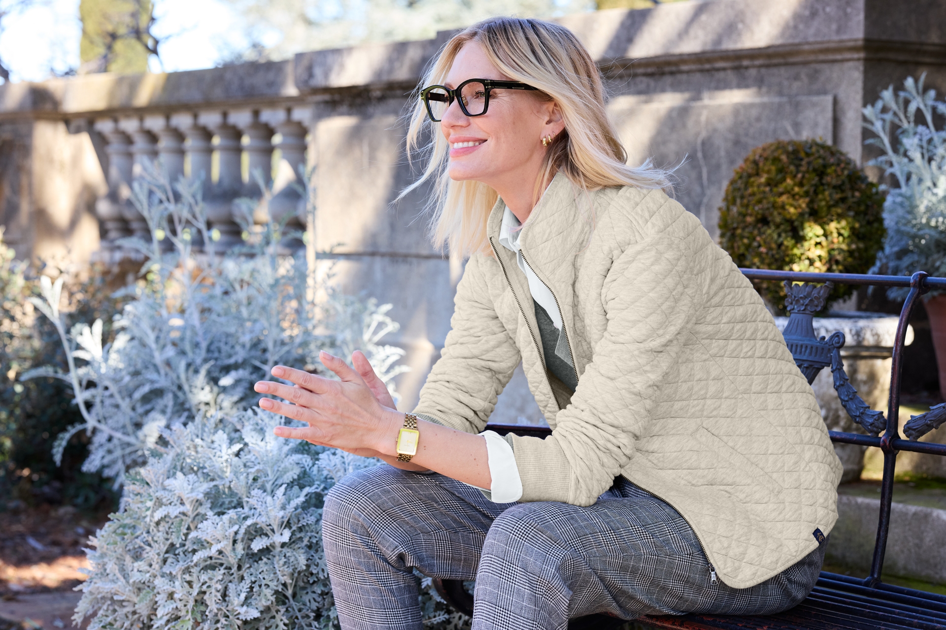 Woman in a Righteous custom-branded quilted jacket sits on a garden bench. 