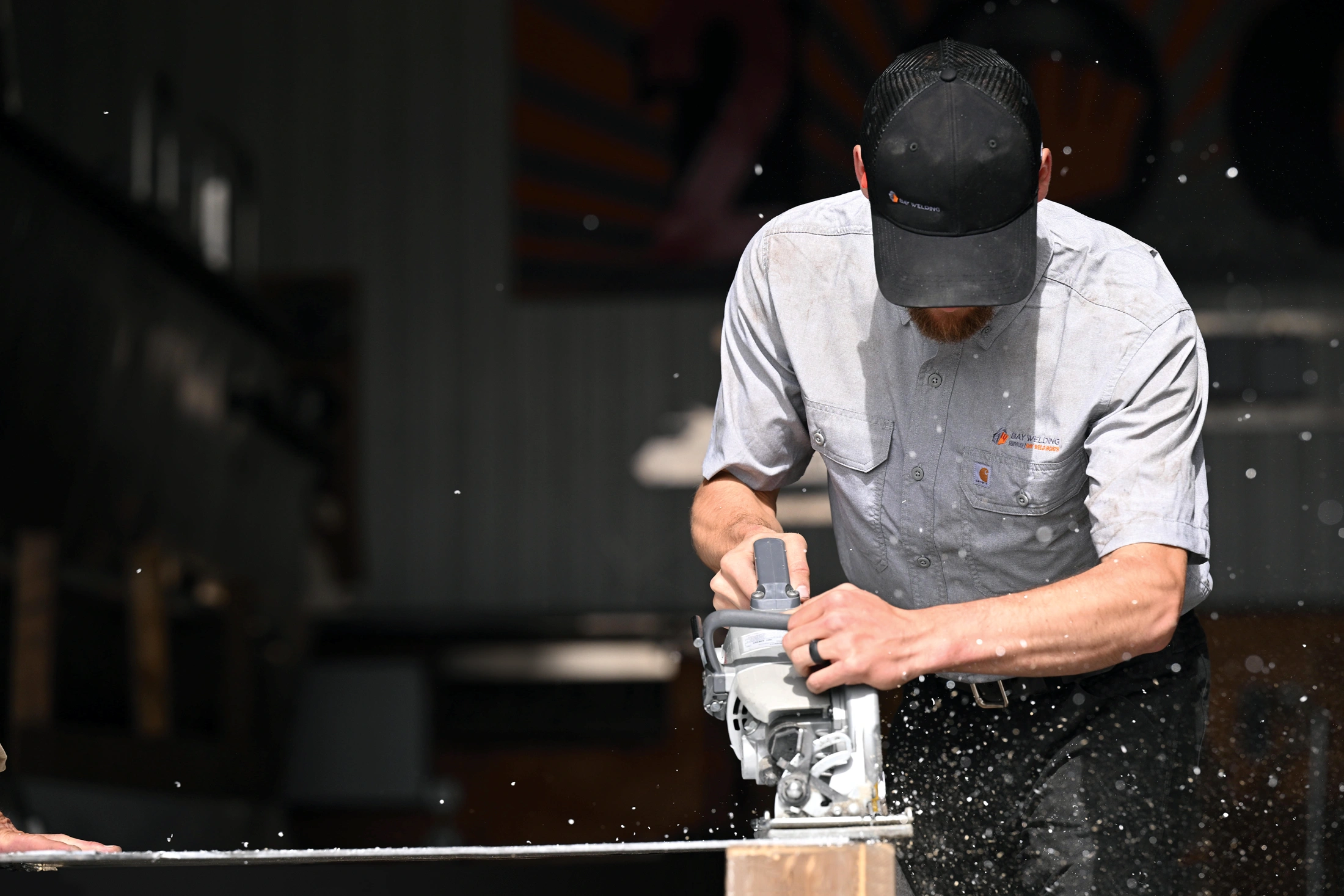 Woodworker wearing a Righteous uniform using a power tool on wood with flying sawdust in a workshop.
