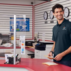 Man in navy polo shirt from Righteous at postal counter holding pencil, smiling at camera in bright facility.