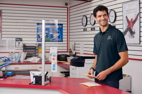 Man in navy polo shirt from Righteous at postal counter holding pencil, smiling at camera in bright facility.